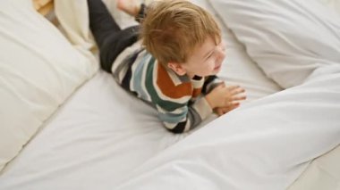 Sarışın çocuk, beyaz bir yatakta, parlak bir yatak odasında oynarken gülüyor..