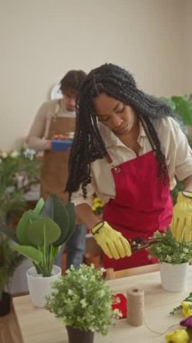 Bir adam ve bir kadın, her ikisi de çiçekçi, kapalı bir çiçekçide birlikte çalışıyorlar, tablet tutan adamla ve bitki düzenleyen kadınla..