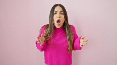 Şaşırmış genç Latin kadın inanılmaz bir şaşkınlık içinde, izole edilmiş pembe bir kazak giyiyor. Korkmuş ama heyecanlı, ağzı korku, şok ve şaşkınlık içinde sonuna kadar açık..