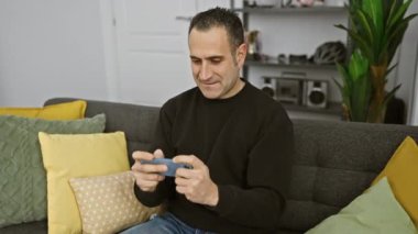 Akıllı telefonuyla meşgul olan bir adam oturma odasındaki kanepede sevinçle kutlama yapar.
