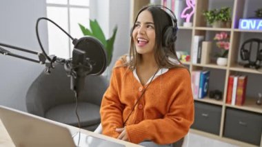 Genç bir İspanyol kadın bir radyo stüdyosunda neşeli bir şekilde şarkı söylüyor, podcast yaparken kendine güveni ve güzelliği yayıyor.