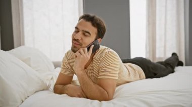Yakışıklı genç adam yatak odasında dinlenirken akıllı telefon kullanıyor, rahat ve rahat bir yaşam tarzını canlandırıyor..