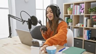 Genç bir İspanyol kadın modern bir radyo stüdyosunda kulaklıkları inceliyor, kapalı bir ortamda podcaster 'ı canlandırıyor..