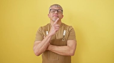 Konsantre olmuş orta yaşlı, gri saçlı bir adam, yüzünde şüphe, önlük ve gözlük, çenesinde parmak, düşüncelere dalmış gözler, güneşli sarı bir zemine karşı izole edilmiş, düşüncelere dalmış..