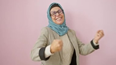 Neşeli orta yaşlı, tesettürlü İspanyol kadın başarıyı kazanan jest ve pembe arka planda heyecanlı çığlıkla kutluyor.