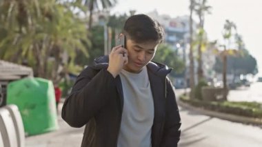 Güneşli şehir caddesini kontrol ederken Asyalı adam akıllı telefondan konuşuyor..