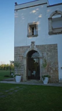 Puglia, İtalya 'da güneşli bir günde bahçesinde yemyeşil yemyeşil bir bahçe bulunan kemerli kapı ve pencereli tarihi taş bina..