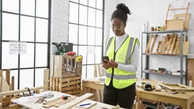 Afrika kökenli Amerikalı kadın telefon kullanıyor ve atölye ortamında notlar alıyor.
