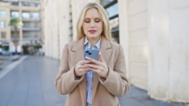 Beyaz kadın şehir caddesinde akıllı telefon kullanıyor.