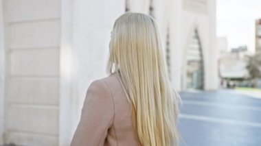 Şık paltolu sarışın bir kadın şehrin ortasında dikilirken gülümsüyor..