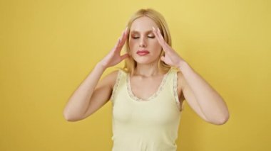 Kolsuz tişört giyen, başı ağrıyan, strese bağlı migreni olan depresyondaki genç sarışın kadın. Sarı arka planda izole edilmiş bir portre