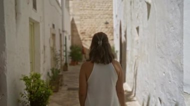 Güzel genç bir kadın Locorotondo, Puglia, İtalya 'nın eski sokaklarında yürüyor, etrafı beyaz evler ve açık Avrupa gökyüzünün altında saksı bitkileriyle çevrili..