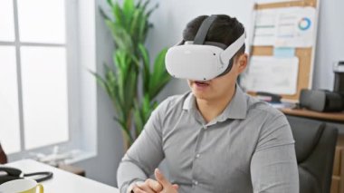Modern ofis ortamında sanal gerçeklik kulaklığı kullanan Asyalı genç adam merak ve yenilikleri ifade ediyor..