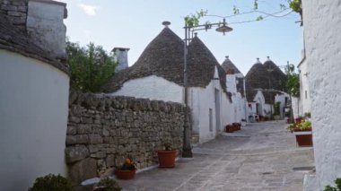 İtalya, Alberobello 'da, mavi gökyüzü altında, tuhaf bir kaldırım taşı caddesi boyunca geleneksel trulli evlerin yer aldığı pitoresk bir sahne..