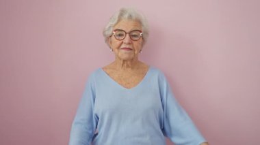 Gri saçlı ve gözlüklü, kendinden emin gülümseyen yaşlı kadın pembe izole edilmiş arka planda kollarını kavuşturuyor. pozitiflik ve güven yayar.