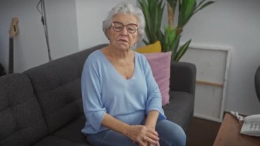 Sırtı ağrıyan yaşlı kadın kanepede oturuyor ve rahatsız görünüyor.