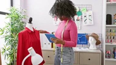 Modern atölyede eskizler ve dikiş aksesuarlarıyla manken yakınında tablet kullanan Afrikalı kadın moda tasarımcısı..