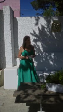 Yeşil elbiseli genç bir İspanyol kadın açık havada Puglia, İtalya 'da beyaz duvarlar ve yeşilliklerle çevrili bir villada kahve içiyor..