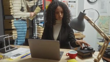 Odaklanmış bir kadın müfettiş telefonda konuşuyor, adam dağınık bir polis ofisinde dosyaları inceliyor, takım çalışması ve suç soruşturmasını resmediyor..