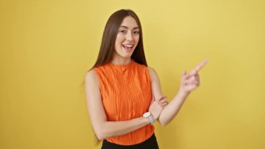 Kolsuz tişörtlü neşeli İspanyol güzeli büyüleyici noktalar içinde ve güneşli sarı izole bir stüdyoda gülümsüyor.