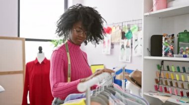 Giysilerle ve dikiş malzemeleriyle çevrili bir butik moda atölyesinde kıyafet karıştıran bir kadın..