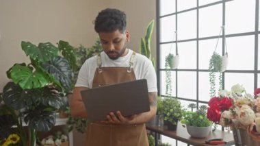 Çiçekçide dizüstü bilgisayar kullanan yakışıklı bir adam. Çiçekler ve buketlerle dolu. Kapalı bir ortam yaratıyor..