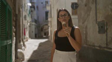 Genç bir İspanyol kadın Puglia, İtalya 'nın eski güzel sokaklarında dondurma külahının tadını çıkarıyor..