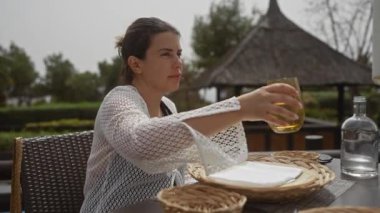 Genç bir kadın, tropik bir tatil köyünde terasta içki içmekten zevk alıyor, rahatlama ve rahatlama hissi yayıyor..