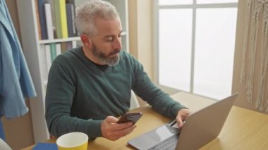 Evde online alışveriş için akıllı telefon ve kredi kartı kullanan sakallı, olgun, beyaz bir adam..