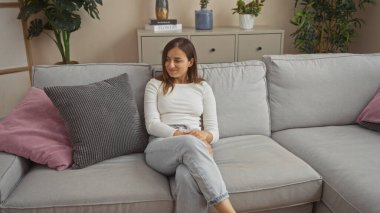 Genç, çekici bir kadın evinin dekore edilmiş oturma odasındaki rahat bir koltuğa rahatça oturur..