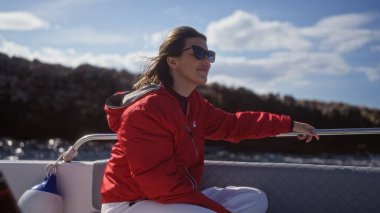 A young hispanic woman in a red jacket enjoying a boat ride in polignano a mare, puglia, italy, with the sea and cliffs in the background. clipart