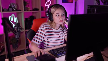 Kulaklıklı genç bir kadın geceleri neon ışıklı bir oyun odasında bilgisayar kullanıyor..