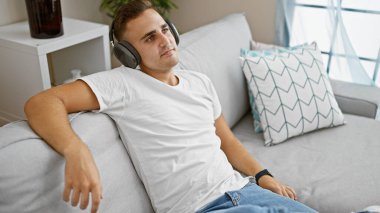 Rahatlamış, kulaklık takan genç bir İspanyol, kanepede uzanıyor, rahatlık ve rahatlık sağlıyor..