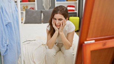 Orta yaşlı bir kadın dağınık bir yatak odasında, gardırop tercihleri veya organizasyonla ilgili endişelerini göstererek stresli görünüyor..