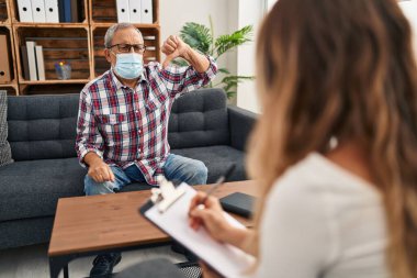 Psikoloji kliniğinde kıdemli kızgın bir adam, yaşlı maskeli, baş parmağıyla sevmediğini belirten bir jest yaparak, morfin etkisinin ortasında olumsuz bir ret işareti veriyor.