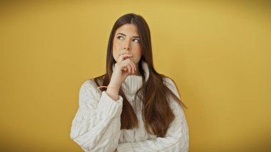 Beyaz süveterli, düşünceli bakışlı, sarı arka planda soyutlanmış, düşünceli bir İspanyol genç kadın..