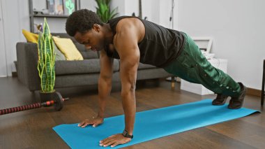 Modern bir oturma odasında mavi bir paspasın üzerinde şınav çeken zinde bir genç.