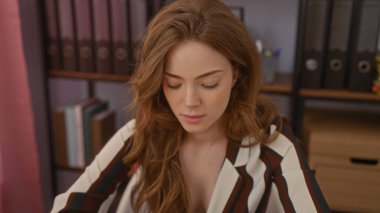 Kitaplar ve dosyalarla dolu raflarla çevrili ev ofis ortamında özenle çalışan çekici sarışın kadın..