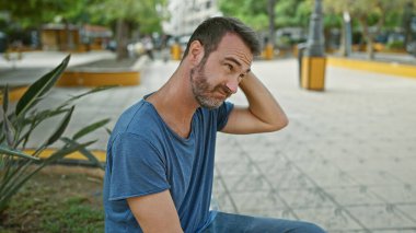 Yakışıklı, orta yaşlı, sakallı, mavi tişörtlü, yeşil yemyeşil bir park ortamında tefekkür eden bir İspanyol..