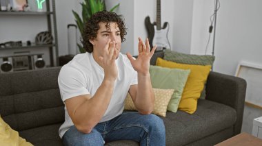 Sıcak bir oturma odasında kanepede oturan kıvırcık saçlı İspanyol genç adam..