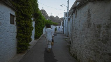 Genç bir İspanyol kadın, Puglia, İtalya 'da geleneksel trulli evlerle çevrili Alberobello' nun eski kasabasının büyüleyici sokaklarında tek başına yürüyor ve sakin bir Avrupa atmosferi yaratıyor..