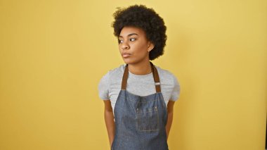 Kıvırcık saçlı, parlak sarı arka planda günlük kıyafetler giyen sakin Afro-Amerikalı kadın..