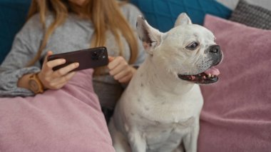 Genç bir kadın oturma odasında dinleniyor, elinde köpek köpeğiyle koltukta dinleniyor..