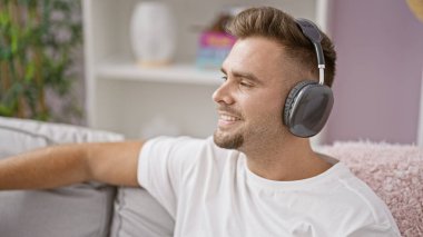 Genç bir İspanyol adam evde rahatlıyor, kulaklıkla müzik dinliyor, rahat, memnun bir hava yayıyor..