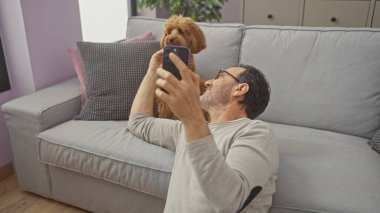 Orta yaşlı İspanyol bir adam ve kanişi modern bir dairenin oturma odasında selfie çekiyorlar..