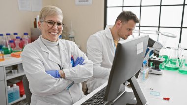 Smiling woman and focused man, both scientists, working together indoors in a modern laboratory. clipart