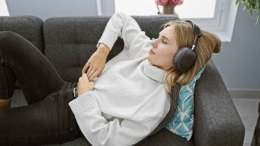 Kapalı bir koltukta uzanan, kulaklıklı, rahat, sarışın bir kadın.