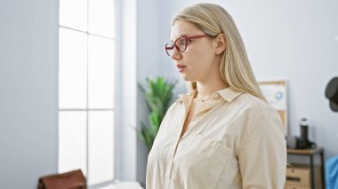 Gözlüklü ve sarı saçlı düşünceli genç bir kadın modern ofis ortamında profesyonelliği ve düşünceli olmayı öneriyor..