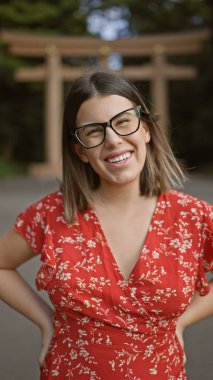 Neşeli, güzel, gözlüklü İspanyol kadın kendinden emin bir şekilde poz veriyor, Tokyo 'nun meiji türbesine gülümsüyor, mutluluğu şaşırtıcı gülüşünün içinden açıkça yayılıyor.