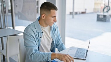 Yakışıklı bir İspanyol, parlak bir üniversite kütüphanesinde dizüstü bilgisayarla çalışıyor.